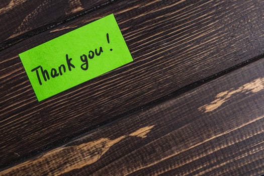 Small green thank you note on brown table close up photo
