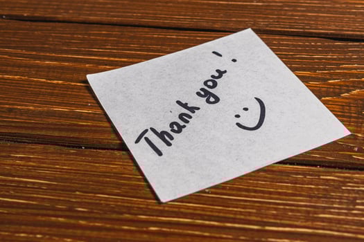 A thank you note is written on a piece of paper and placed on a wooden surface. photo