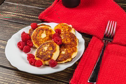 Cottage cheese pancakes with fresh raspberries on a white plate on the table photo