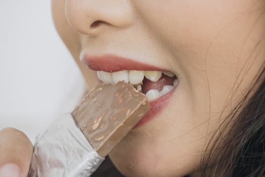 Close up portrait of Asian woman eating a chocolate bar while smiling as she enjoys her snack. photo
