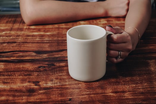 Woman's hand is holding a white coffee cup while sitting by a wooden dining table. photo