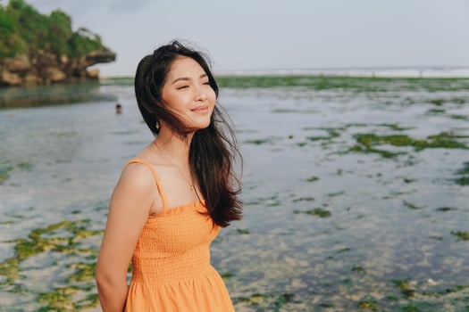 Happy young Asian woman in a yellow dress is smiling and standing by the beach. photo