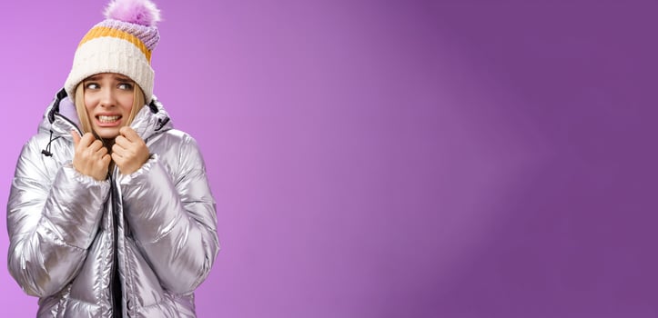 Freezing uncomfortable trembling cute blond girl in hat pull jacket tight feeling cold walking snowy mountains low temperature clenching teeth stooping shaking, standing upset purple background photo