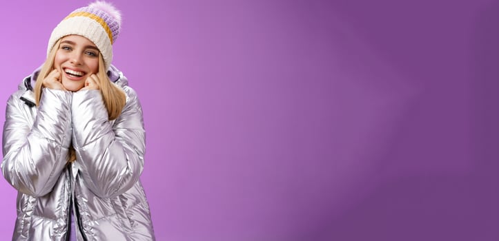Delighted charming tender female in stylish cute hat silver shiny jacket lean chin hands smiling sighing enjoying watching lovely romantic scene wanna fall in love standing happily purple background photo