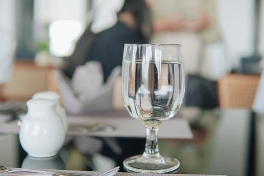 A glass of water sits on a table with a napkin and a salt shaker, set in a restaurant or a cafe. photo