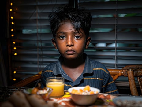 A young boy sits at a table, thoughtfully looking at the camera photo
