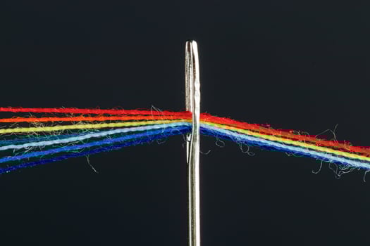 multi-colored threads for sewing in the form of a rainbow pass through an antique needle on a black background photo