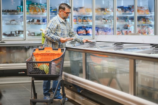Bearded man with frozen fish his hands stands at the refrigerator in the department of frozen food photo
