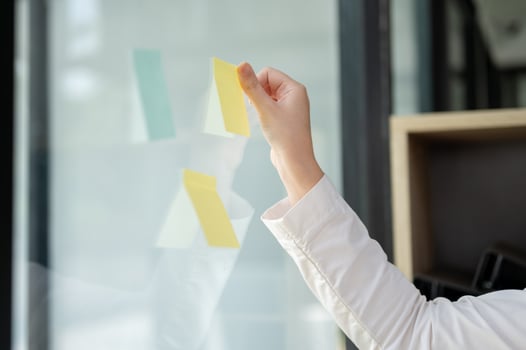 A close-up image of a businesswoman attaching a sticky note to a glass wall in the office. photo