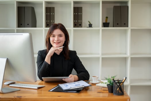 A beautiful businesswoman in a black suit sitting at her desk in a minimal, bright office. photo