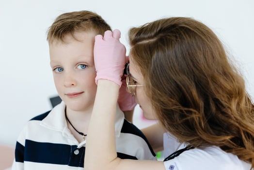 Female doctor examining boy's ear with otoscope in office. Ear cavity treatment health checkup photo