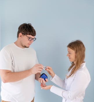 young male patient testing hearing aid in clinic exam room, female doctor helping photo