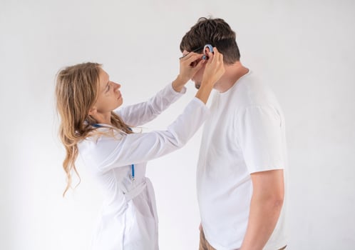young male patient testing hearing aid in clinic exam room, female doctor helping photo