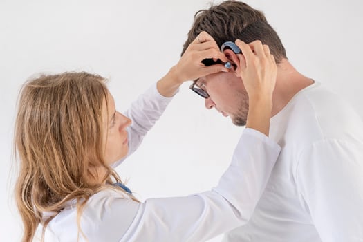 young male patient testing hearing aid in clinic exam room, female doctor helping photo
