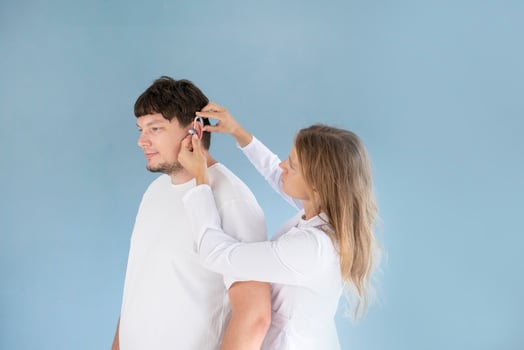 young male patient testing hearing aid in clinic exam room, female doctor helping photo
