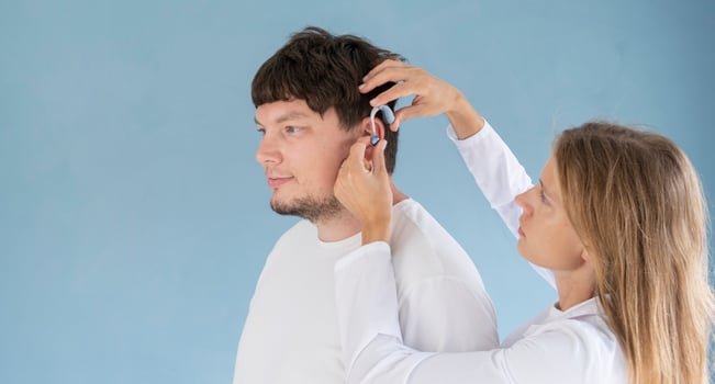 young male patient testing hearing aid in clinic exam room, female doctor helping photo