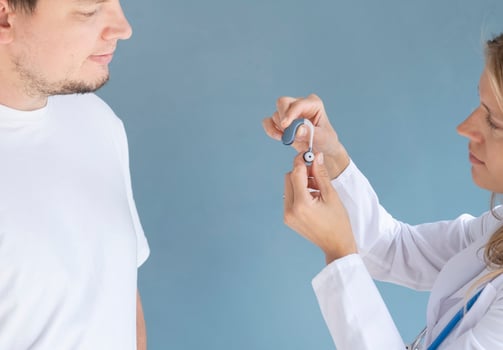 young male patient testing hearing aid in clinic exam room, female doctor helping photo