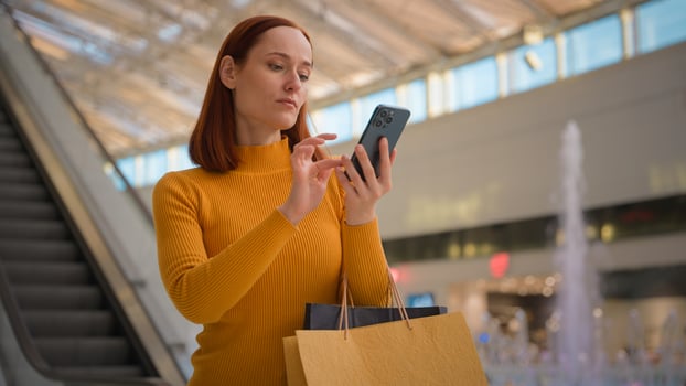 Serious confused Caucasian business woman female girl tourist customer businesswoman holding mobile phone device internet store app searching in paper bags card money buy online indoors shopping mall photo