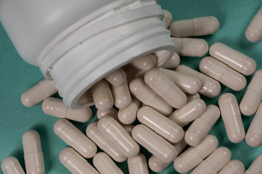 bottle of pills, some of which spilled onto a light blue surface photo