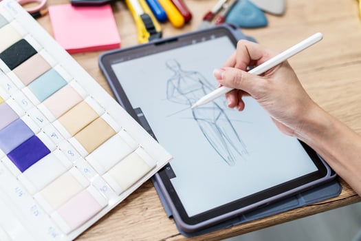 Hand Fashion designer woman draws sketches for a new fashion design, draws on an electronic tablet fashionable clothes. Close up female actively working workspace photo