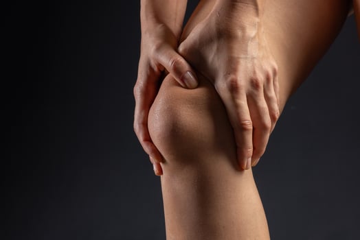 woman hands close up pressing on knee joint on dark background, knee pain concept photo