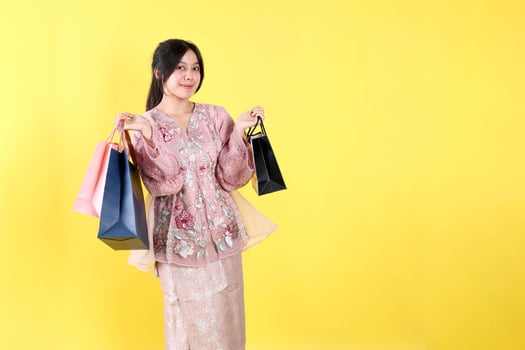 Cheerful Indonesian Asian Woman Wearing Kebaya, Holding Various Color of Paper Bag. photo