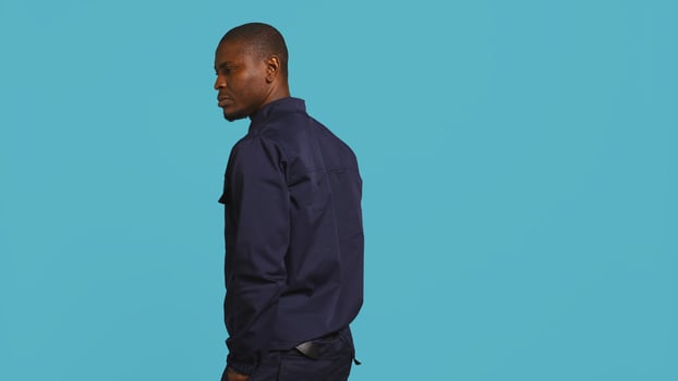 Portrait of security guard overseeing premises to prevent intrusion hearing suspect sounds, turning around. Private law enforcement worker standing isolated with back against studio backdrop, camera B photo
