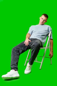 Young Man Seated on White Chair Posing Confidently Against Green Background photo