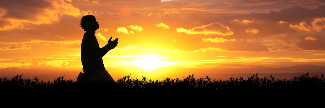 Silhouette of a Person Praying at Sunset with a Vibrant Orange and Yellow Sky in the Background photo