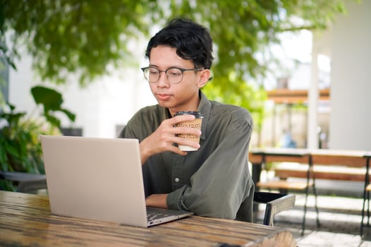 Asian man working on laptop at the outdoor cafe. A man working on laptop with a cup of coffee. photo