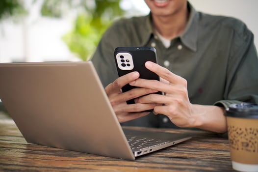 Man holding smartphone while working on his laptop. Asian male focused on his phone and laptop at the outdoor cafe photo