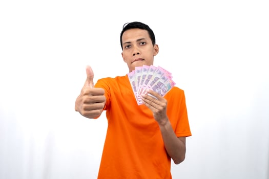 Portrait of a young Asian man wearing an orange t-shirt with a happy, surprised, pleased expression while carrying hundreds of thousands of rupiah. isolated on a white background. photo