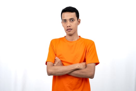 Portrait of a young Asian man wearing a colored t-shirt posing upright with his two arms crossed over his stomach. Isolated on a white background. photo