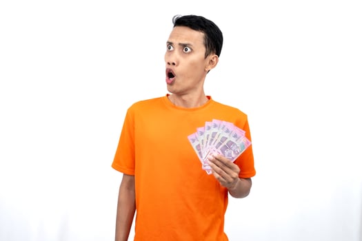 Portrait of a young Asian man wearing an orange t-shirt with a happy, surprised, pleased expression while carrying hundreds of thousands of rupiah. isolated on a white background. photo