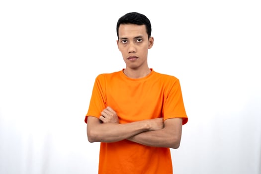 Portrait of a young Asian man wearing a colored t-shirt posing upright with his two arms crossed over his stomach. Isolated on a white background. photo