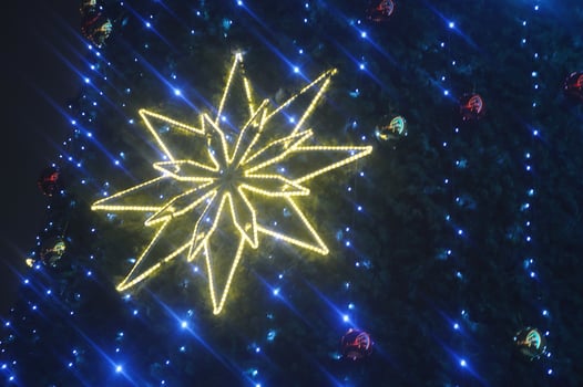 Glowing snowflake, Christmas star on blue festive lights of tree. Festive New Year background. Modern illumination on city street photo