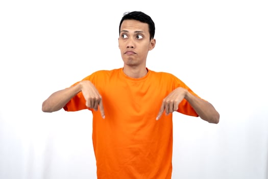 Portrait of a young Asian man wearing an orange t-shirt pointing down copy space for promotional space. isolated on white background. photo