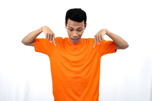 Portrait of a young Asian man wearing an orange t-shirt pointing down copy space for promotional space. isolated on white background. photo