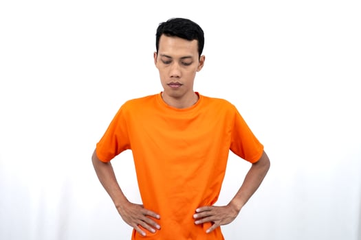 Portrait of a young Asian man wearing a colored t-shirt looking tired and lethargic with his hands on his hips. Isolated on white background. photo