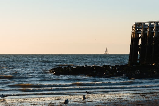 A serene coastal scene at sunset featuring a sailboat on the horizon, gentle waves, and a wooden pier. photo