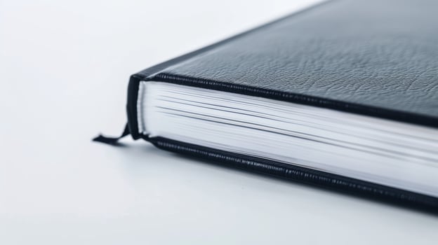 Black leather-bound thick book resting on white surface, displaying its blank pages photo