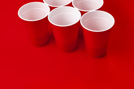 Cups and plastic ball on red background. Beer pong game photo