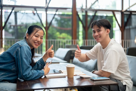 Two positive, happy young Asian college students are doing homework together at a coffee shop. photo