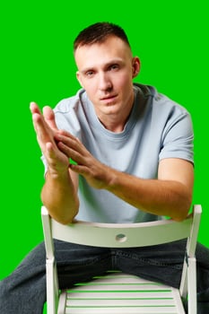 Young Man Seated on White Chair Posing Confidently Against Green Background photo