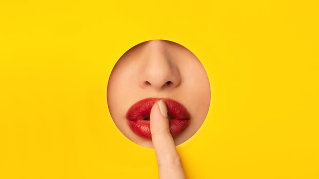 A close-up view of a woman gently touching her red lips on a bright yellow background. The contrast between the colorful backdrop and the soft texture of the lips creates a simple yet impactful image. photo