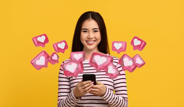 Cute cheerful pretty young asian woman wearing casual clothing holding cell phone, texting her boyfriend, using dating mobile app, yellow studio background photo