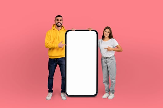 A man and woman standing together, pointing at a blank phone screen with focused expressions. They seem to be discussing something on the device and are engaged in the topic. photo