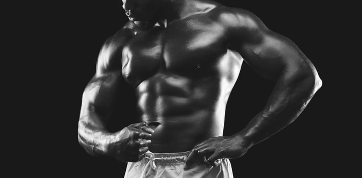 A muscular man flexes his defined physique in a black and white image against a dark background, highlighting his muscles. photo