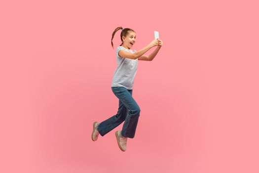 A young girl is captured mid-air, jumping energetically with a cell phone in hand. She appears joyful and carefree as she leaps into the sky with a mobile device. photo