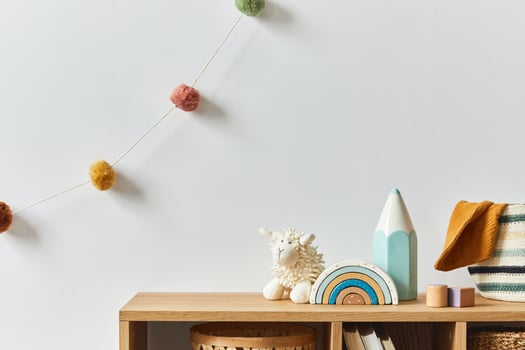 Stylish scandinavian newborn baby room with toys, plush animal, photo camera and accessories. Cozy decoration and hanging cotton balls on the white wall.